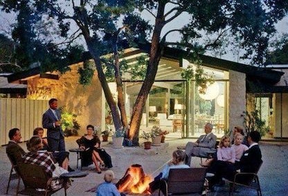 People sitting around backyard fire pit in a Cliff May home